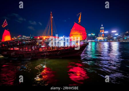 Superbe vue nocturne d'une jonque illuminée dans le port Victoria en face de l'horizon fantastique de Hong Kong avec ses impressionnants gratte-ciel Banque D'Images