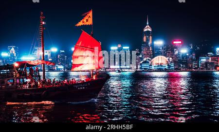 Superbe vue nocturne d'une jonque illuminée dans le port Victoria en face de l'horizon fantastique de Hong Kong avec ses impressionnants gratte-ciel Banque D'Images