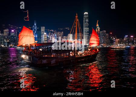Superbe vue nocturne d'une jonque illuminée dans le port Victoria en face de l'horizon fantastique de Hong Kong avec ses impressionnants gratte-ciel Banque D'Images