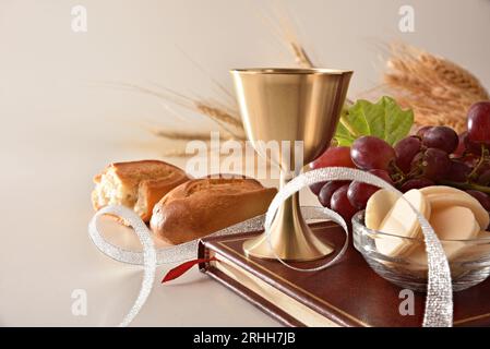 Coupe de vin et hôtes sur la bible pour eucharistie avec du pain et des raisins de décoration autour sur la table blanche et fond isolé blanc. Vue avant. Banque D'Images