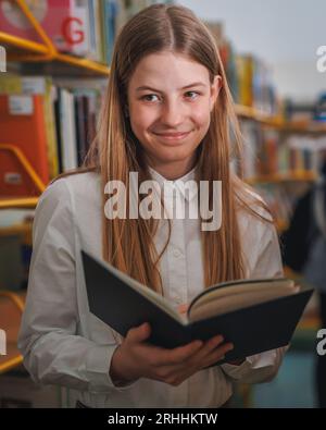 Écolière cherchant et choisissant des livres dans une étagère dans la bibliothèque. Éducation, littérature et nouveaux concepts d'édition. Banque D'Images