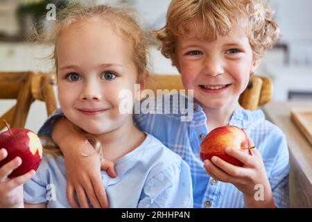 Souriant garçon mignon avec le bras autour de la sœur mangeant des pommes à la maison Banque D'Images