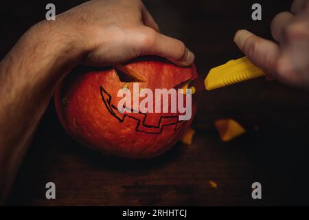 La citrouille Halloween de Jack. Les mains de l'homme sculptent la bouche avec un couteau en papier. Image avec mise au point sélective . Photo de haute qualité Banque D'Images