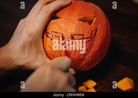 La citrouille Halloween de Jack. Les mains de l'homme sculptent la bouche avec un couteau en papier. Image avec mise au point sélective . Photo de haute qualité Banque D'Images