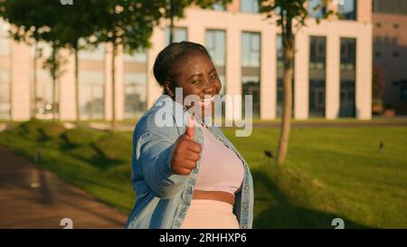 Enthousiaste heureux succès afro-américain ethnique étudiante fille satisfaite femme à l'extérieur de la ville montrant comme pouce vers le haut consentement approbation d'accord comme Banque D'Images
