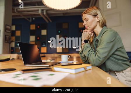 Femme d'affaires fatiguée pensant comment résoudre le problème avec le projet pendant le travail sur ordinateur portable dans le coworking Banque D'Images