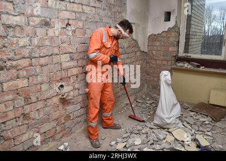 Constructeur nettoyant l'appartement après les travaux de démolition, portant des gants, un masque, des bottes et des combinaisons orange. Banque D'Images