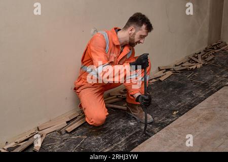 Menuisier enlevant les vieilles planches de parquet en bois dans la maison. Bâtisseur en combinaisons orange. Banque D'Images