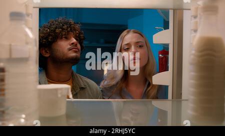 Point de vue POV à l'intérieur du réfrigérateur fille caucasienne femme petite amie femme et homme arabe gars indien petit ami mari multiracial couple la nuit Banque D'Images