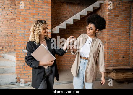 agent immobilier avec dossier donnant les clés de la nouvelle maison à un client afro-américain débordé de joie Banque D'Images