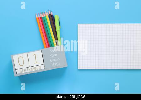 01 septembre. Image d'un calendrier en bois pour septembre 1 sur une table bleue, vue de dessus. Retour à l'école. Calendrier, crayons et cahier ouvert Banque D'Images