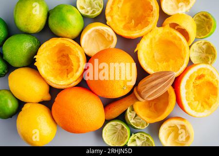 Agrumes entiers et jus avec un alésoir à agrumes en bois : centrifugeuse manuelle entourée d'oranges entières et coupées en deux, de citrons et de citrons verts Banque D'Images