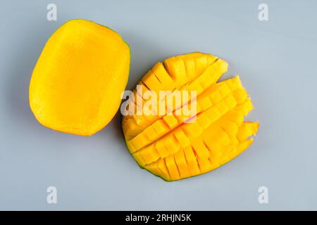 Moitiés de mangue évidée coupées et non coupées sur fond bleu : moitié d'une mangue coupée en dés avec l'autre moitié non coupée Banque D'Images