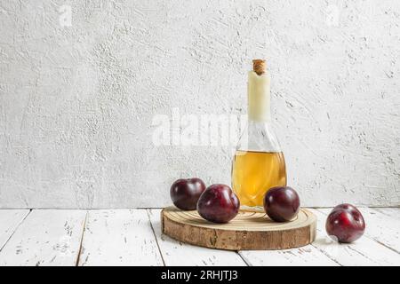 Rakija ou rakia slivovica - eau-de-vie traditionnelle de prunes des Balkans dans la bouteille et prunes fraîches sur le fond clair Banque D'Images