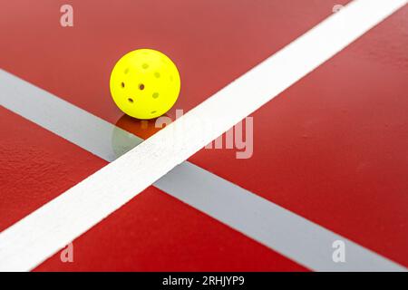 Un pickleball sur un court de tennis de pickleball rouge humide avec des lignes blanches combinées avec des lignes de pickleball grises Banque D'Images