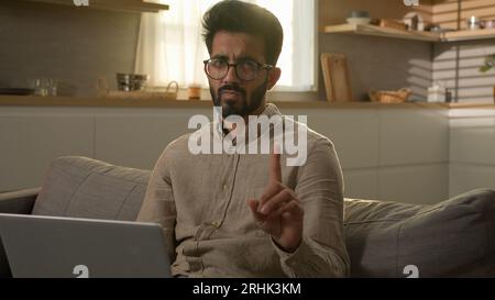Homme indien arabe homme d'affaires freelance travaillant avec un ordinateur portable de la cuisine à la maison gars insatisfait sur le canapé agitant index doigt négatif signe d'avertissement non Banque D'Images