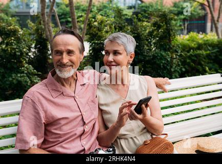 Couple de retraités souriants assis sur un banc dans un parc Banque D'Images