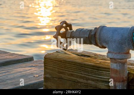 Robinet d'eau extérieur, bavoir de tuyau, sur un poteau en bois à un quai pendant le coucher du soleil. Banque D'Images