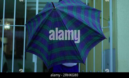 Homme senior ouvrant parapluie pour protéger de la pluie, sort dans la rue de la maison. Personne âgée quittant la résidence, ouvre la porte marche dans le trottoir urbain Banque D'Images