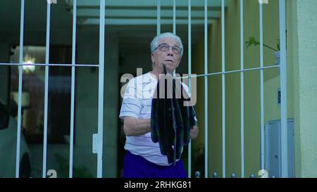 Homme senior ouvrant parapluie pour protéger de la pluie, sort dans la rue de la maison. Personne âgée quittant la résidence, ouvre la porte marche dans le trottoir urbain Banque D'Images