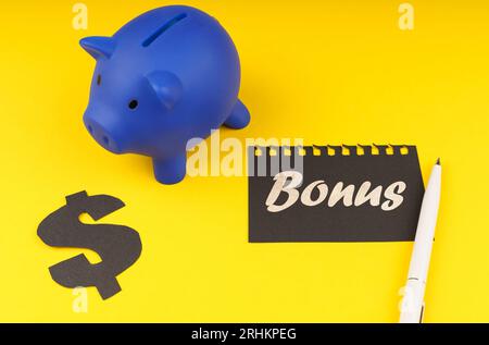 Concept commercial. Sur un fond jaune, il y a une tirelire, à côté se trouve un symbole du dollar et une feuille d'un bloc-notes avec l'inscription - bonus Banque D'Images