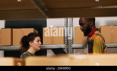 Équipe de superviseurs vérifiant la liste des stocks et faisant l'inventaire dans la salle d'entreposage, personnes diverses vérifiant la logistique pour la distribution des marchandises. Homme et femme examinant les produits. Prise de vue à main levée. Banque D'Images