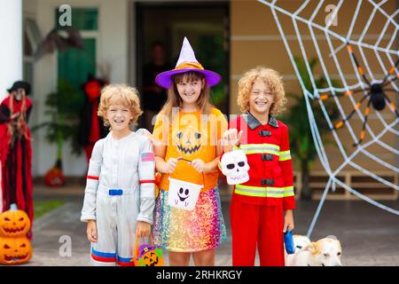 Les enfants trichent ou gâtent le soir d'Halloween. Les enfants habillés à la porte de la maison décorée. Garçon et fille en costume de sorcière et de vampire et chapeau Banque D'Images