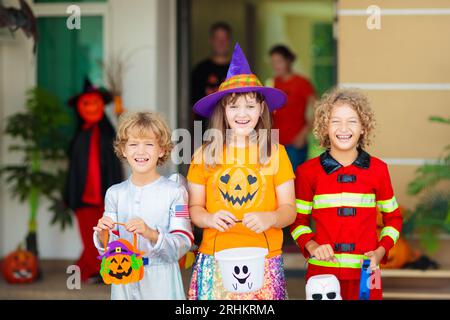 Les enfants trichent ou gâtent le soir d'Halloween. Les enfants habillés à la porte de la maison décorée. Garçon et fille en costume de sorcière et de vampire et chapeau Banque D'Images