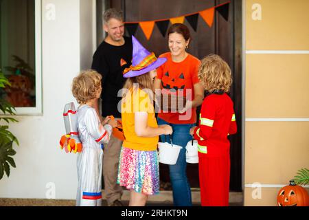 Les enfants trichent ou gâtent le soir d'Halloween. Les enfants habillés à la porte de la maison décorée. Garçon et fille en costume de sorcière et de vampire et chapeau Banque D'Images