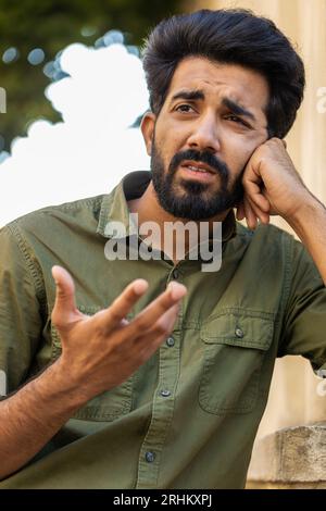 Triste homme indien malheureux pense aux préoccupations de la vie, souffre d'une situation injuste. Problème, se sentir mal, agacé, épuisement, chagrin. Frustré déprimé arabe musulman solitaire dans la rue de la ville. Vertical Banque D'Images
