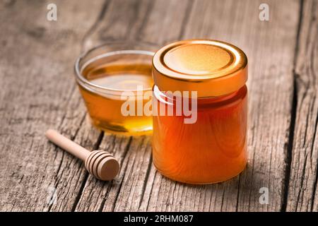 Miel bio dans un bocal en verre fermé et dans un bol en verre transparent, godet en bois sur un fond en bois rustique, gros plan. Banque D'Images