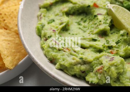 Bol de délicieux guacamole avec des chips de citron vert et nachos sur la table, gros plan Banque D'Images