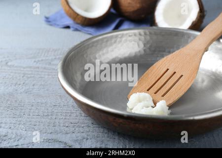 Poêle à frire avec huile de cuisson de noix de coco bio et spatule sur table en bois gris, gros plan Banque D'Images