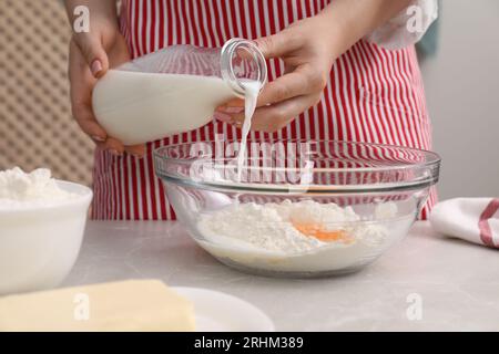 Préparer de savoureux baklava. Femme versant du lait dans un bol avec de la farine et des œufs à la table gris clair, gros plan Banque D'Images