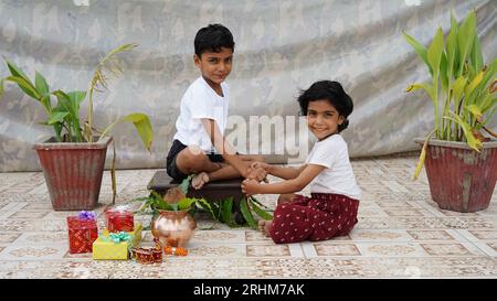 Fille heureuse attachant rakhi sur le poignet de son frère assis isolé sur fond de studio Banque D'Images