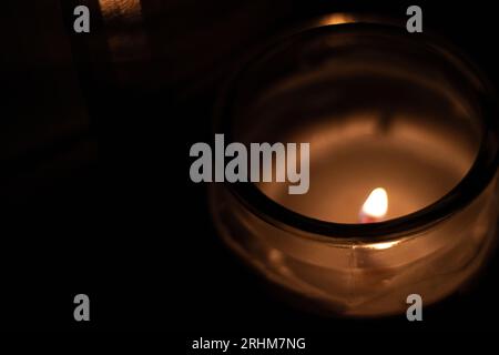 Gros plan de la flamme de bougie dans un pot transparent - tir en grand angle. Gros plan de la flamme brûlant sur la bougie, isolé sur un fond noir. Flamme de bougie Banque D'Images