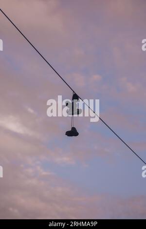 Vieilles baskets guirlande accrochées à un fil électrique contre le ciel et les nuages. Culture moderne des adolescents. Banque D'Images