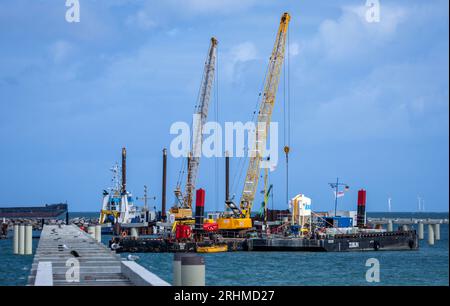 Prerow, Allemagne. 10 août 2023. Des grues sont utilisées pour assembler des structures en béton pour le nouveau port de l'île en face de la plage de la mer Baltique. Des sections de construction cruciales pour le nouveau port de l'île ont déjà été achevées et toutes les piles de soutien nécessaires pour la jetée ont été installées. Le port de l'île devrait ouvrir pour la saison des sports nautiques 2024 comme prévu. Le port en forme de goutte remplacera à l'avenir le port d'urgence de Darßer Ort. Crédit : Jens Büttner/dpa/Alamy Live News Banque D'Images