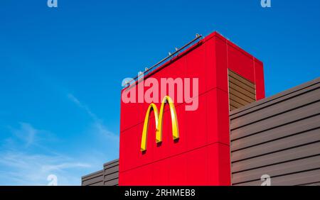 Voûtes dorées populaires de McDonald's sur un fond bleu ciel de panneau extérieur rouge. Partie du bâtiment rouge avec le logo de la succursale McDonalds à Vancouver Cana Banque D'Images