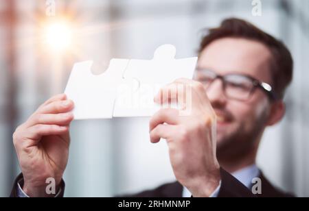 Portrait d'un homme d'affaires optimiste tenant des pièces de puzzle, résolvant des problèmes, regardant la caméra, portant un costume noir. Banque D'Images