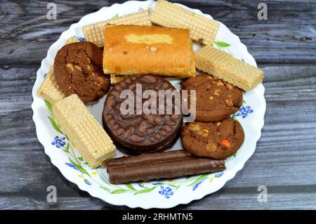 Une assiette de bonbons avec des bâtonnets de chocolat, des gaufrettes croquantes avec garniture à la crème au chocolat, des biscuits croquants garnis de vanille, du gâteau roulé suisse garni Banque D'Images