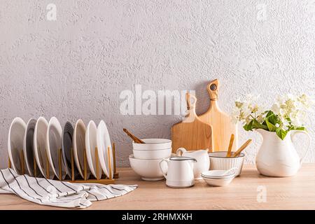 un ensemble d'assiettes dans le sèche-linge et divers bols en céramique sur un comptoir en bois. Carafe blanche avec des fleurs. Intérieur élégant d'un espace cuisine moderne Banque D'Images