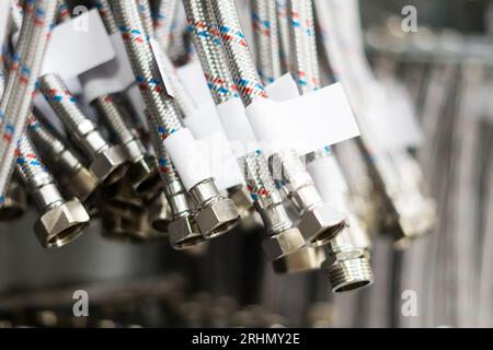 Tuyau flexible en acier inoxydable tressé fermé disposé en rangée contre un mur blanc. Banque D'Images