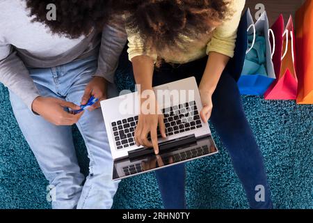 Jeune couple Shopping Online sur ordinateur portable avec des sacs multicolores sur canapé Banque D'Images