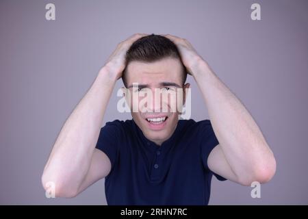 Jeune homme exprimant la douleur, tenant la tête dans les mains, concept de mal de tête sur fond isolé Banque D'Images