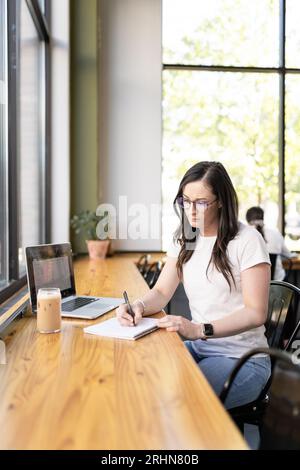 Une femme buvant du café glacé écrit dans son cahier Banque D'Images