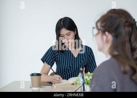 Groupe d'étudiants asiatiques sourire et lire un livre pour les étudiants discutant des devoirs ou étudier l'anglais assis au bureau dans la salle de classe Banque D'Images