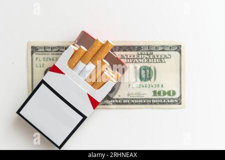 Paquet de cigarettes sur une photo de billets de cent dollars. Concept de coût élevé du tabagisme Banque D'Images