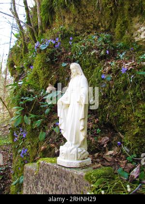 Statuette de la vierge marie et fleurs et mousse sur les rochers derrière Banque D'Images