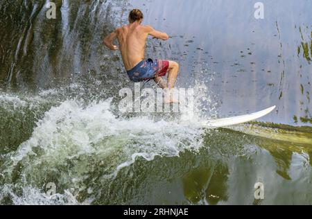 18 août 2023, Bavière, Munich : un surfeur tombe dans l'eau de la vague de surf Floßlände près de la rivière Isar dans le sud de la capitale bavaroise après un tour sur sa planche. Photo : Peter Kneffel/dpa Banque D'Images